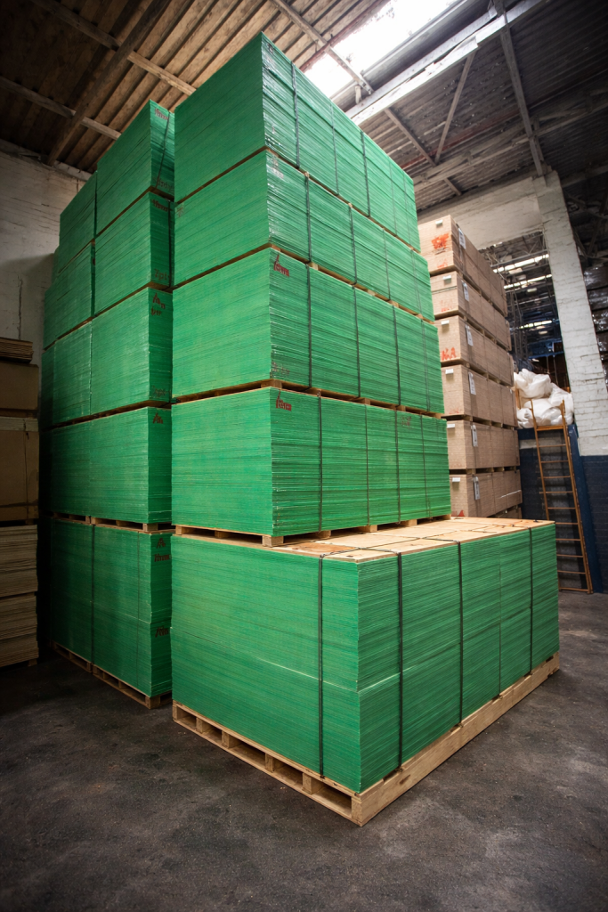 Stacks of green plywood shutter ply sheets stored on pallets in a factory warehouse for construction and formwork applications.